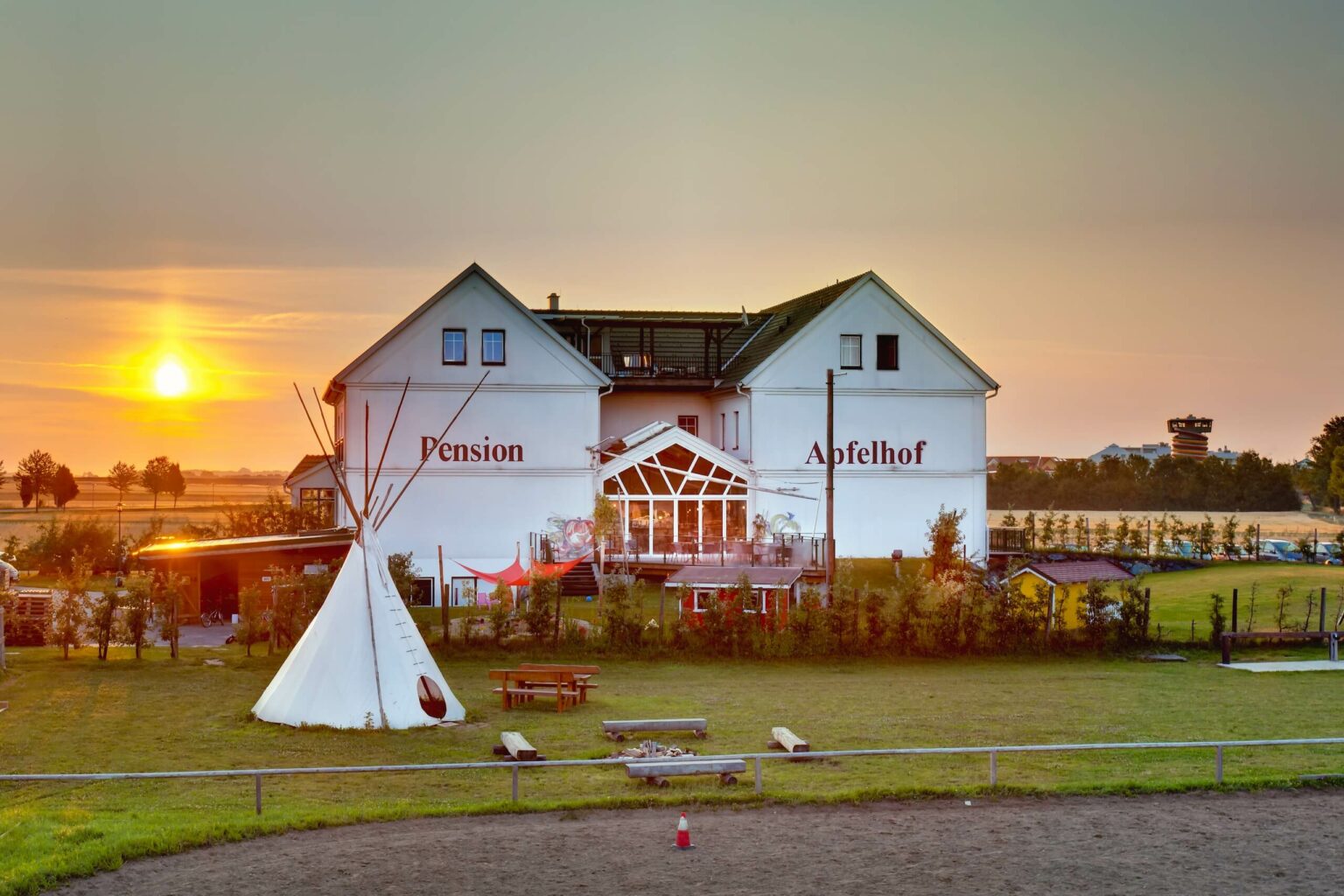 Weißes Gebäude mit großem Garten und Tipi-Zelt im Sonnenuntergang